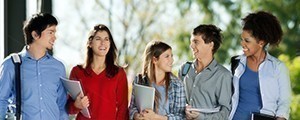 An image of 5 students with books, talking in a group